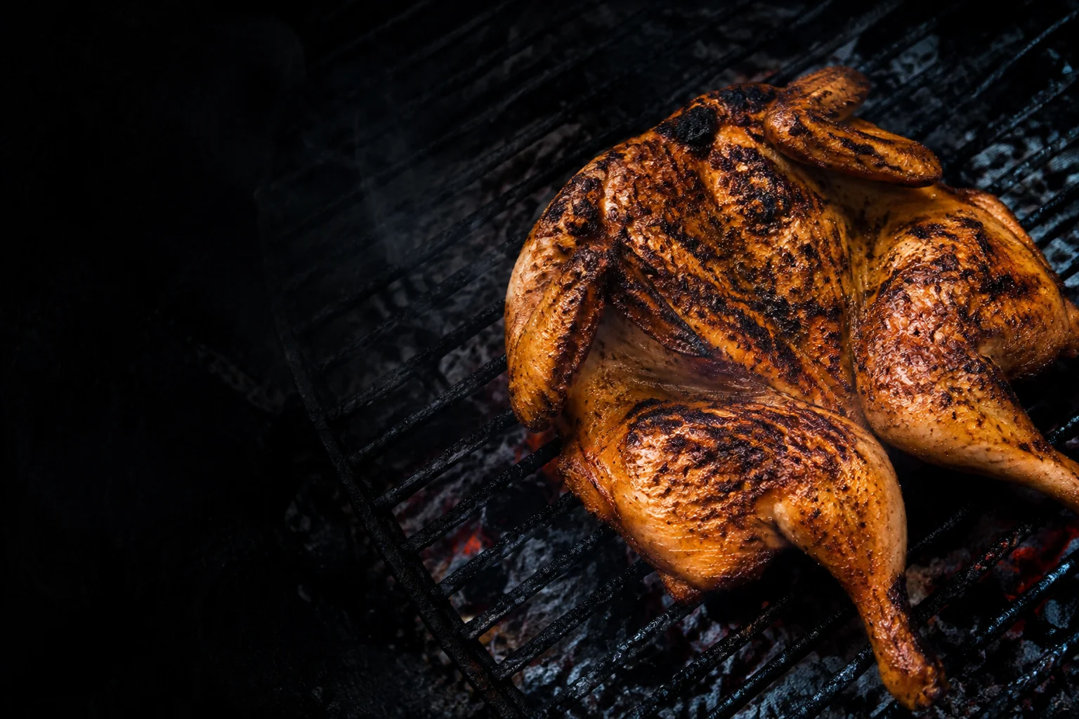 Charcoal-grilled chicken with golden skin and deep grill marks over glowing coals.